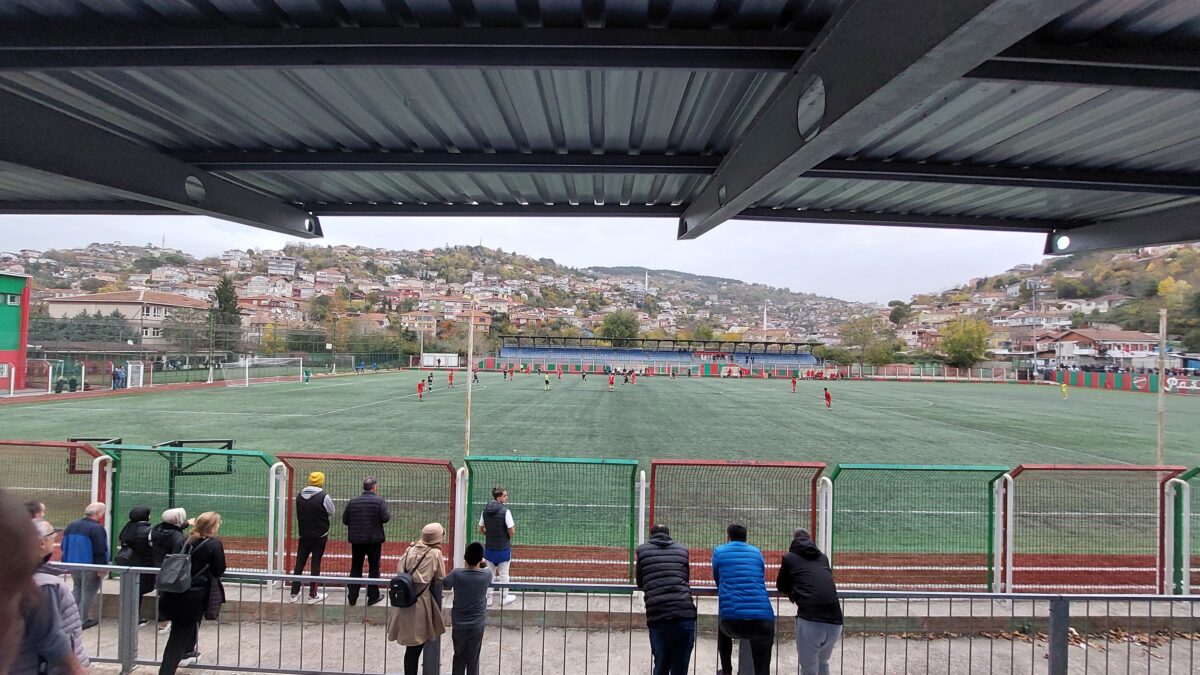 Bir amatör futbol maçından genel görünüm; tribünde izleyiciler ve sahada oyuncular (temsili görsel)